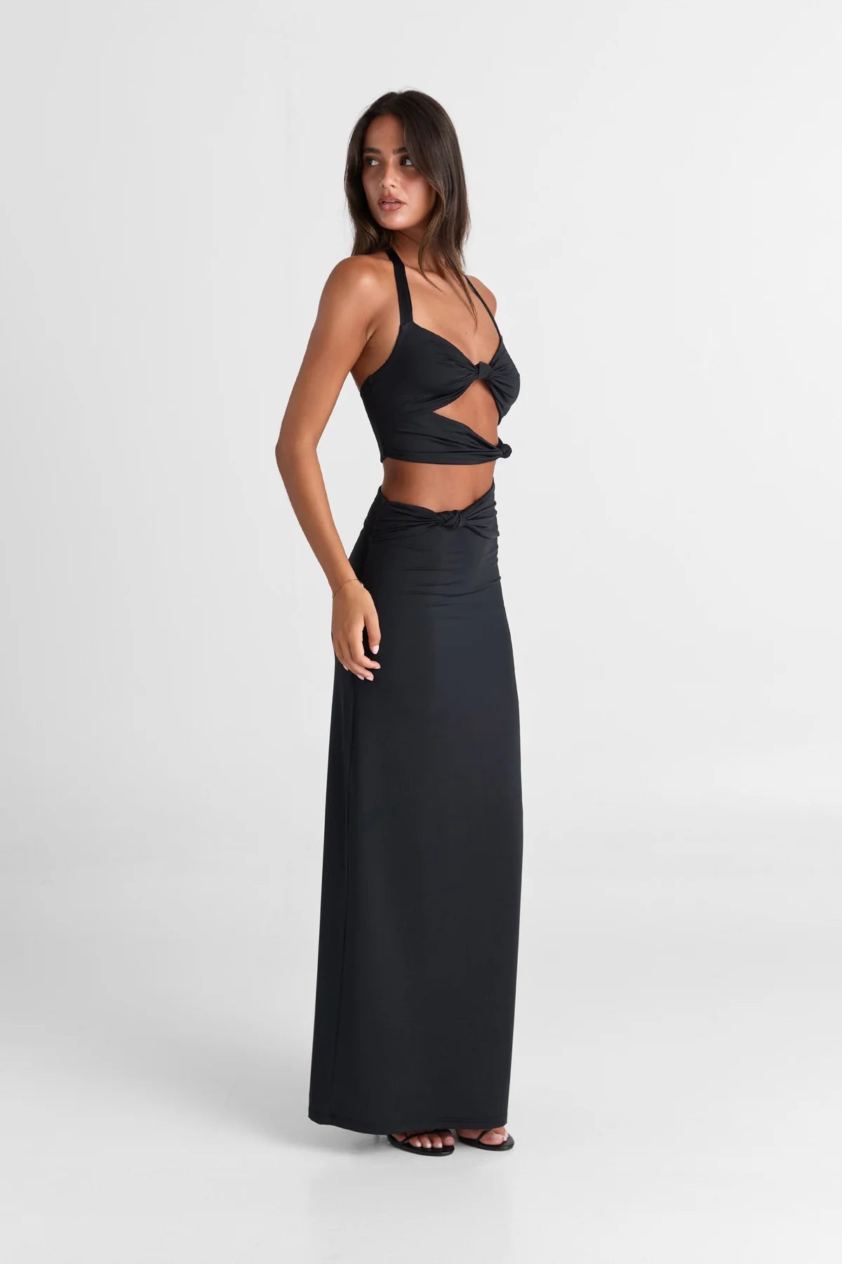 Side profile of Sasha Therese Oralia Maxi Dress in black showing body skimming fit and flowing floor length silhouette